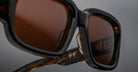 Close-up of Jacques Marie Mage Nakahira tortoiseshell sunglasses with brown lenses, featuring gold Chinese characters on the inner arm, set against a neutral gray background.