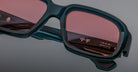 Close-up of Jacques Marie Mage Nakahira sunglasses with thick, dark green frames and rose-tinted lenses; “Handcrafted in Japan” and Japanese characters are visible on the inner arm.