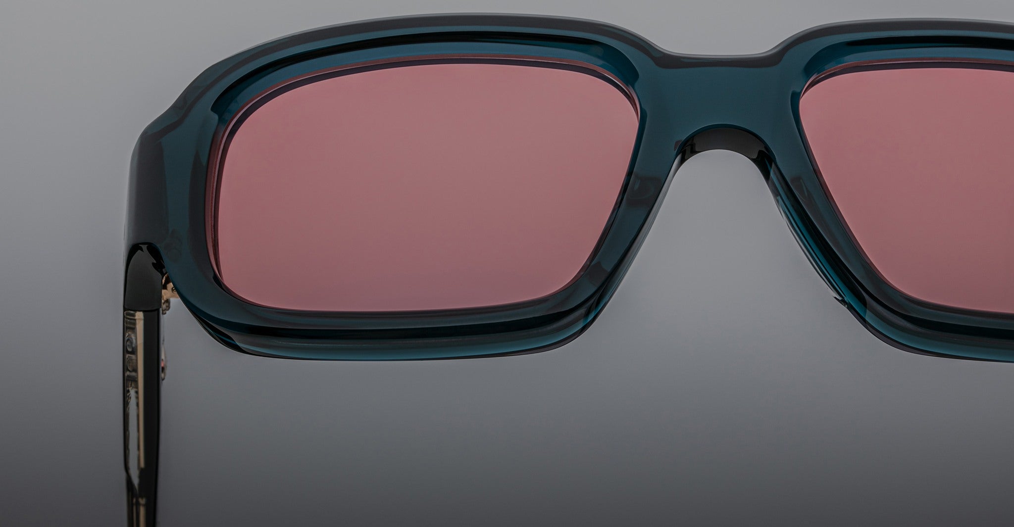Close-up of Jacques Marie Mage Nakahira rectangular sunglasses featuring dark green frames and pink-tinted lenses, set against a plain gray background.