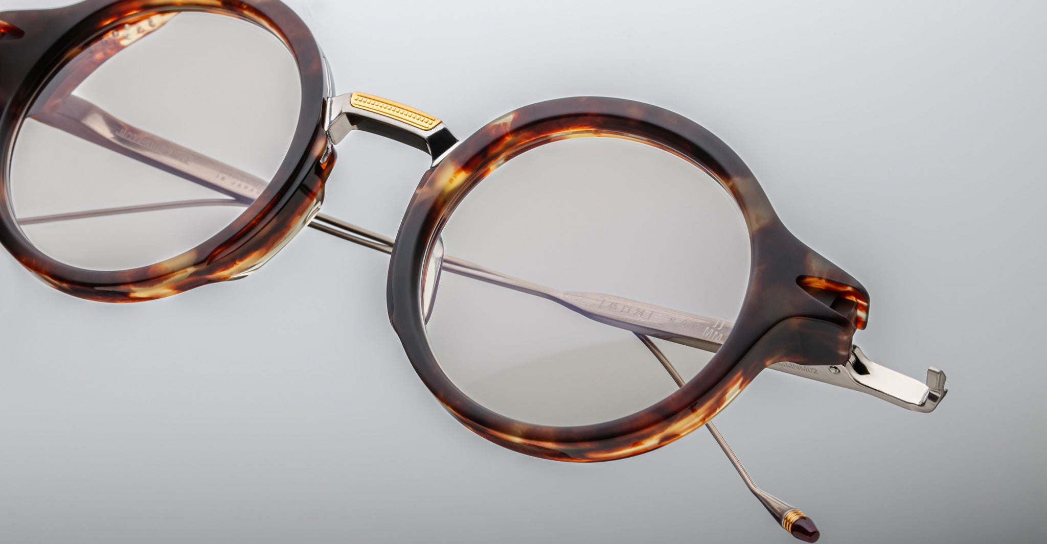 Close-up of Jacques Marie Mage Norman round eyeglasses in tortoiseshell with gold hinges and thin metal arms, frontal view.