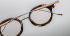 Jacques Marie Mage Norman round tortoiseshell eyeglasses with gold accents and slim metal arms, shown from a front angle.