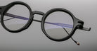 Jacques Marie Mage Norman round black eyeglasses with thick frames and one detached temple arm, front angle view.