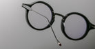 Close-up of Jacques Marie Mage Norman black round eyeglasses, side angle showing one temple arm extended.