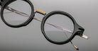 Jacques Marie Mage Norman round black eyeglasses with metal bridge and temples, close-up angle.