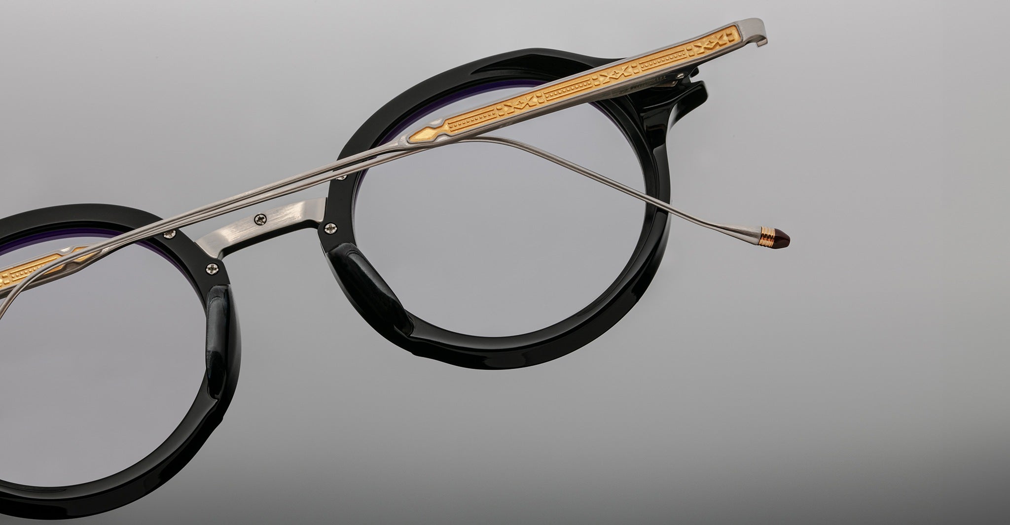 Jacques Marie Mage Norman eyeglasses, black round frame with gold and silver arms, front view.