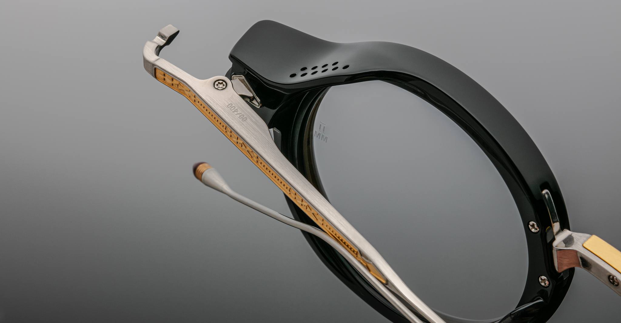 Close-up of Jacques Marie Mage Norman eyeglasses, black frame, metal temples with yellow and silver accents, front angle.