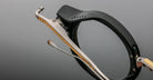 Close-up of Jacques Marie Mage Norman eyeglasses, black frame, metal temples with yellow and silver accents, front angle.