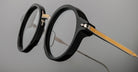 Close-up of Jacques Marie Mage Norman round black eyeglasses with gold patterned arms, showing front and side details.
