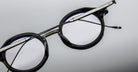 Close-up of Jacques Marie Mage Norman round eyeglasses in black with silver arms, showing front and side details.