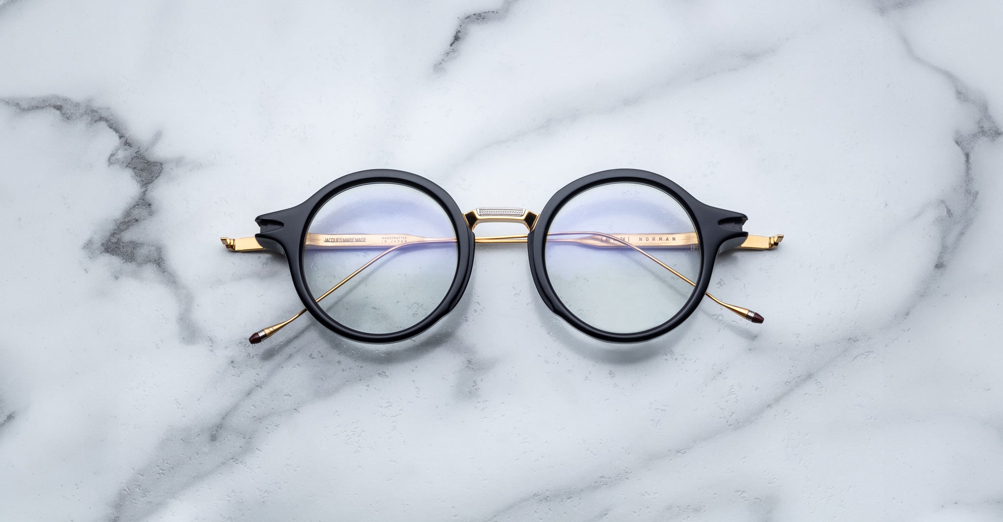 Jacques Marie Mage Norman round black eyeglasses with gold arms, top-down view.