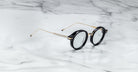 Jacques Marie Mage Norman eyeglasses with round black frames and gold temples, shown from the front.