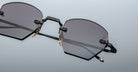 A close-up of Jacques Marie Mage Oatman hexagonal rimless sunglasses, featuring dark tinted lenses, slim black and gold arms, and a jewel at the temple tip, set against a plain light background.