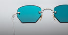 Close-up of Jacques Marie Mage Oatman eyewear: blue-tinted, angular lenses and metallic frames, inspired by signature Jacques Marie Mage design, displayed on a neutral background.