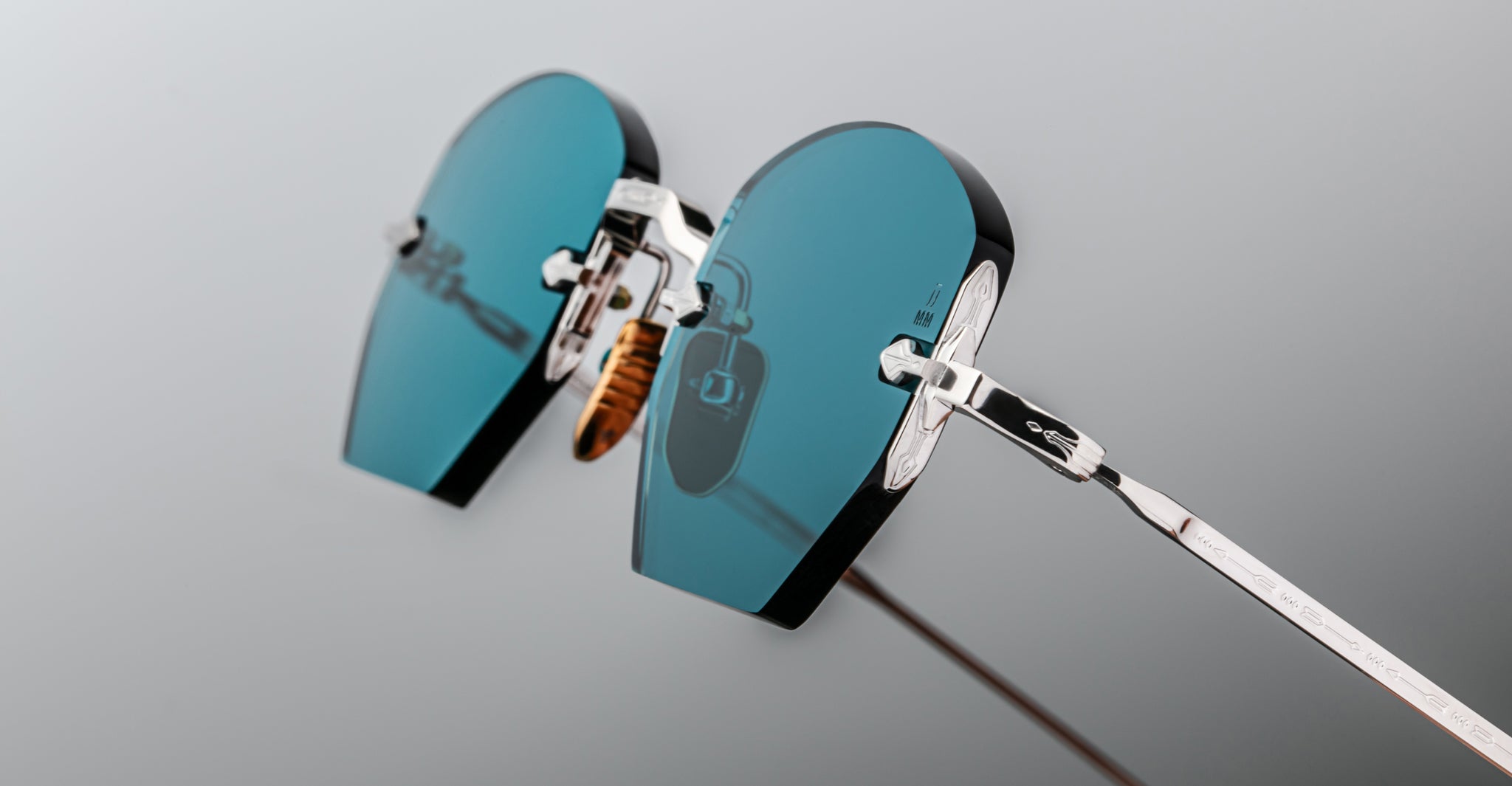 Close-up of Jacques Marie Mage Oatman by Jacques Marie Mage, featuring heart-shaped, teal-tinted lenses and silver metal frames inspired by handmade Japanese eyewear, set against a neutral background.