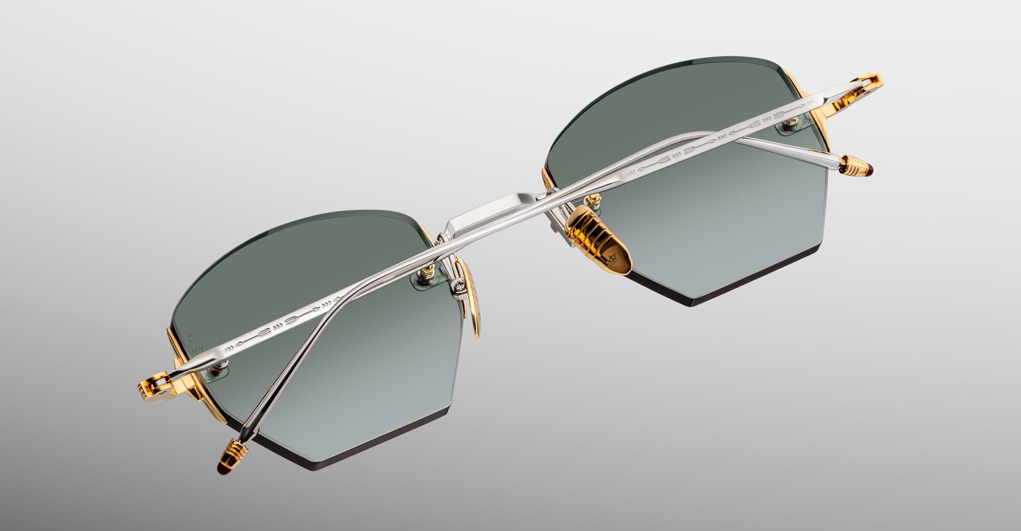 Jacques Marie Mage Oatman sunglasses with rimless, geometric green-tinted lenses and gold and silver metal arms, viewed from above against a neutral background.
