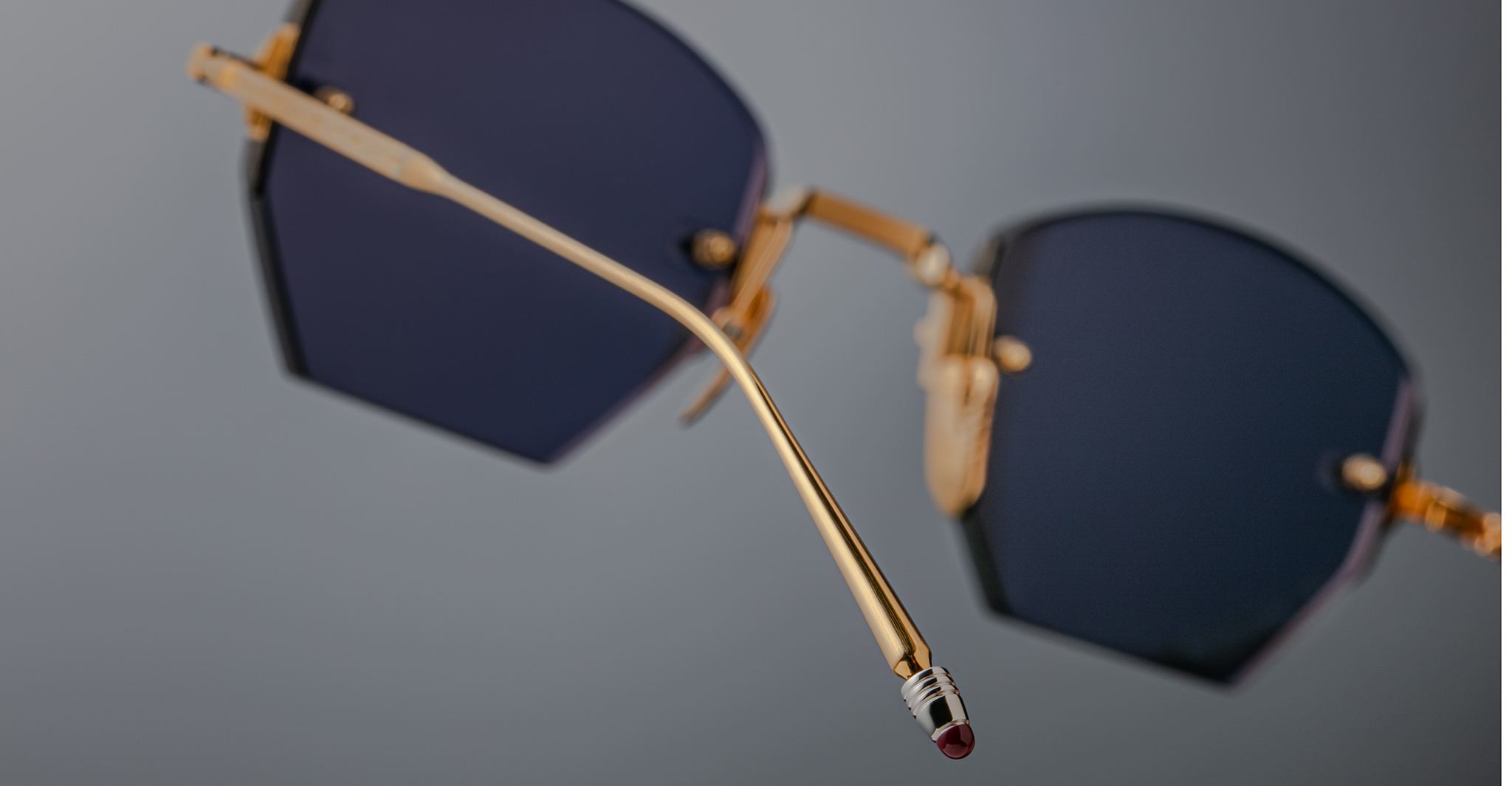 Close-up of Jacques Marie Mage Oatman hexagonal rimless sunglasses with gold frames and dark lenses, showcasing the detailed temple arm against a neutral background.
