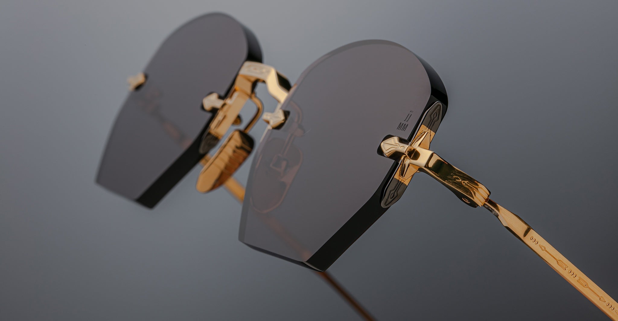 Close-up of Jacques Marie Mage Oatman hexagonal rimless sunglasses with dark geometric lenses and gold frames, highlighting exquisite handmade Japanese craftsmanship against a neutral background.