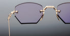 Close-up of Jacques Marie Mage Oatman hexagonal rimless sunglasses with gold metal frames and purple-tinted lenses, highlighting the craftsmanship of handmade Japanese eyewear by Jacques Marie Mage against a gradient background.