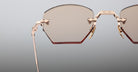 Close-up of the upper half of Jacques Marie Mage Oatman hexagonal rimless sunglasses, featuring gold metal frames and lightly tinted lenses, highlighting the refined elegance of Jacques Marie Mage against a light gray background.