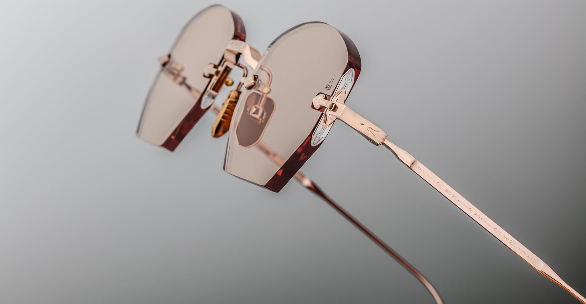 Close-up of Jacques Marie Mage Oatman hexagonal rimless sunglasses featuring rose gold metal temples and light pink-tinted lenses, displayed on a neutral background.