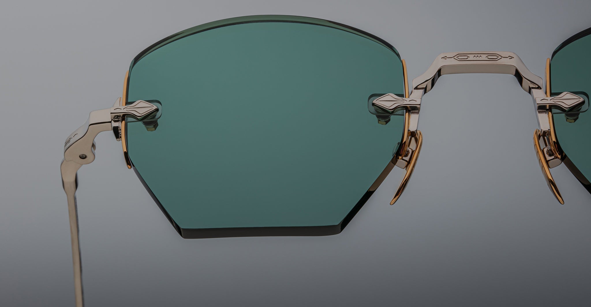 Close-up of Jacques Marie Mage Oatman rimless hexagonal sunglasses with green-tinted geometric lenses and gold frames, highlighting the artistry of handmade Japanese eyewear against a plain background.