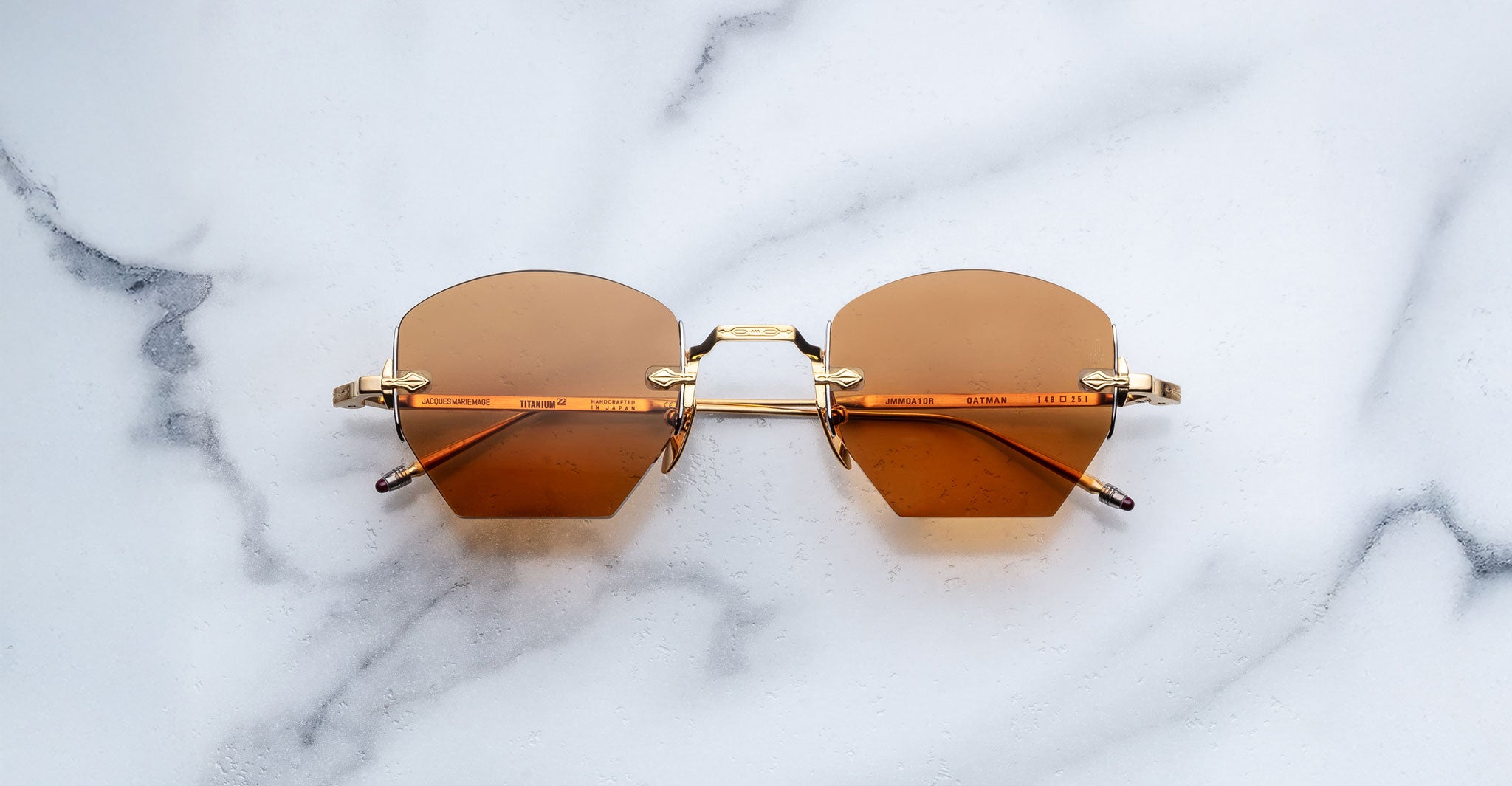 Jacques Marie Mage Oatman in Suntan geometric sunglasses with gold frames and brown-tinted lenses, shown from above on a flat surface.