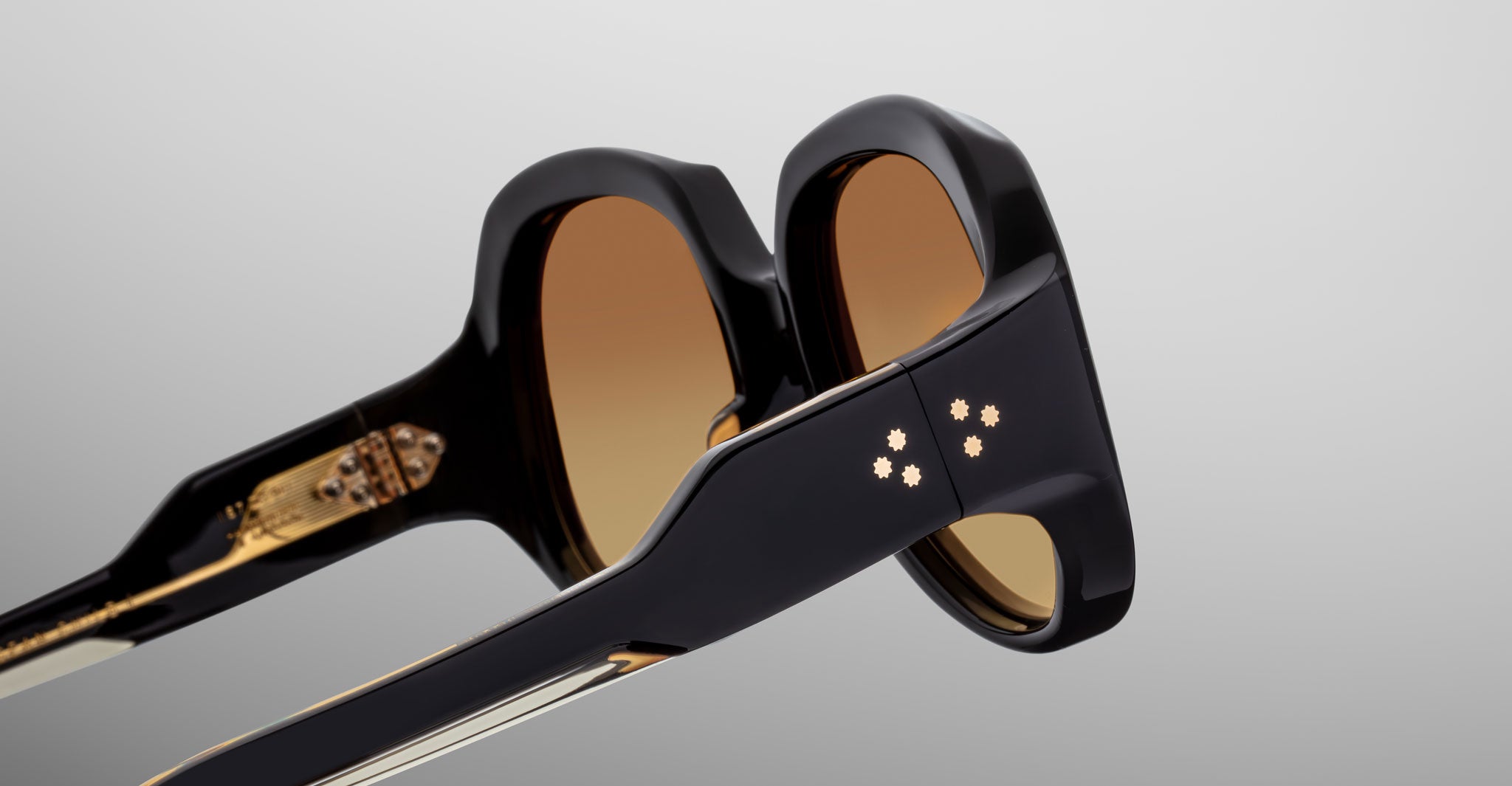 Close-up of Jacques Marie Mage Ocean Child black sunglasses with brown tinted lenses and three star-shaped metal accents on thick side arms, set against a plain light background.