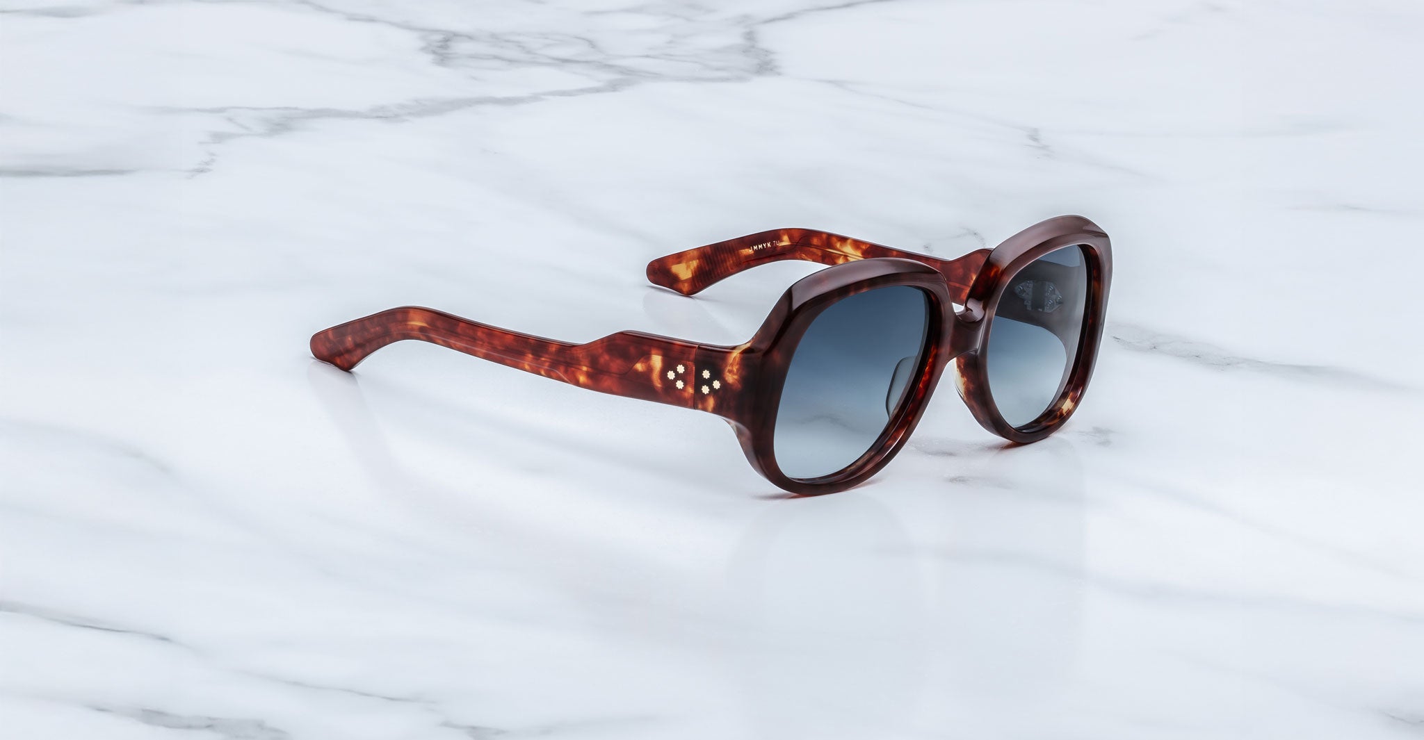Jacques Marie Mage Ocean Child tortoiseshell sunglasses with dark, rounded lenses displayed on a white marble surface.