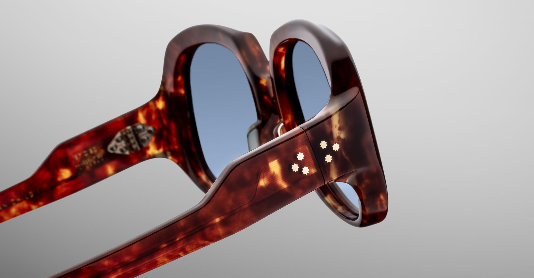 Close-up of Jacques Marie Mage Ocean Child sunglasses in tortoiseshell, featuring blue-tinted lenses and small white star-shaped accents on the arms, highlighting frame details against a plain background.