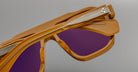 Close-up of three pairs of Jacques Marie Mage Octavian sunglasses with orange frames and purple lenses, stacked to display the frame details and metallic arms, set against a plain gray background.