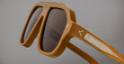 Close-up of Jacques Marie Mage Octavian oversized square sunglasses with a thick matte brown frame and dark lenses. The temples have a white accent with 3 small star rivets near the hinge, set against a plain gray background.