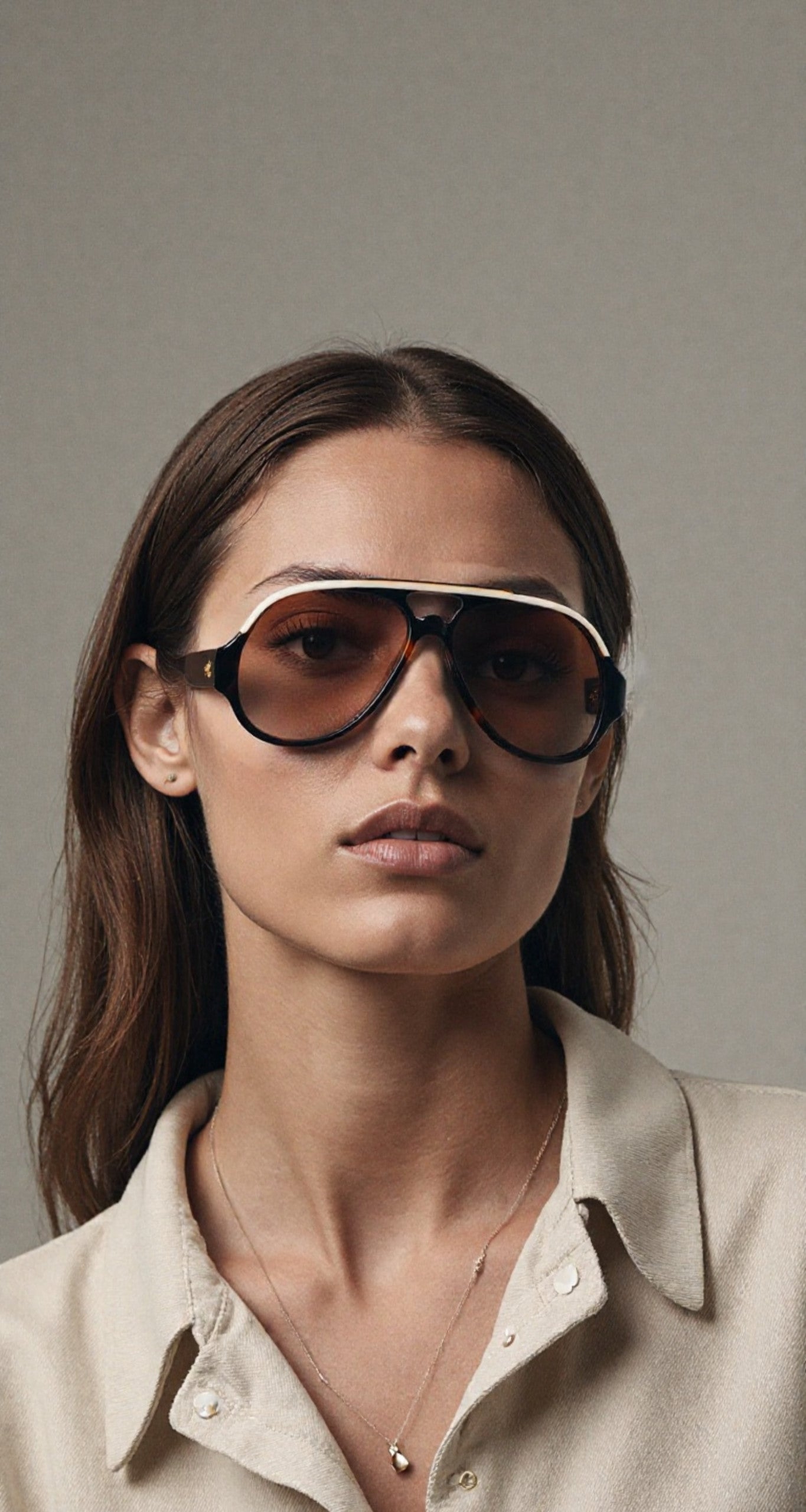 Close-up of a model wearing Jacques Marie Mage Orion sunglasses in Havana, with a bold, oversized design in warm brown tones and gold accents, styled with a beige shirt and delicate jewelry
