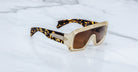 Jacques Marie Mage Pausa sunglasses feature a gold frame and tortoiseshell arms, displayed from an overhead angle.