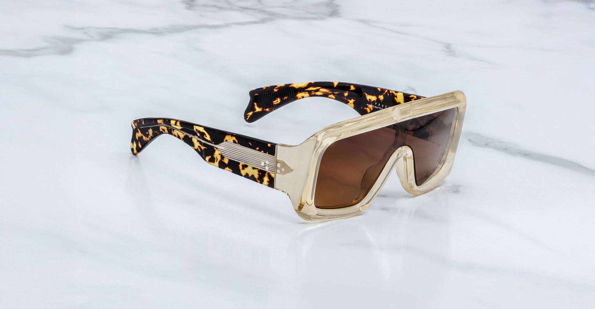 Jacques Marie Mage Pausa sunglasses feature a gold frame and tortoiseshell arms, displayed from an overhead angle.