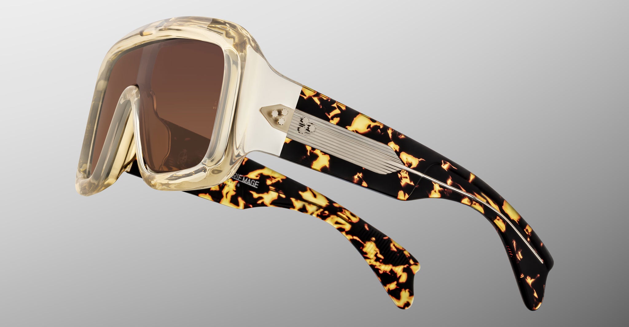 Jacques Marie Mage Pausa sunglasses with clear and tortoiseshell frames, wide brown UV lenses, and metal accents on the temples, front view.