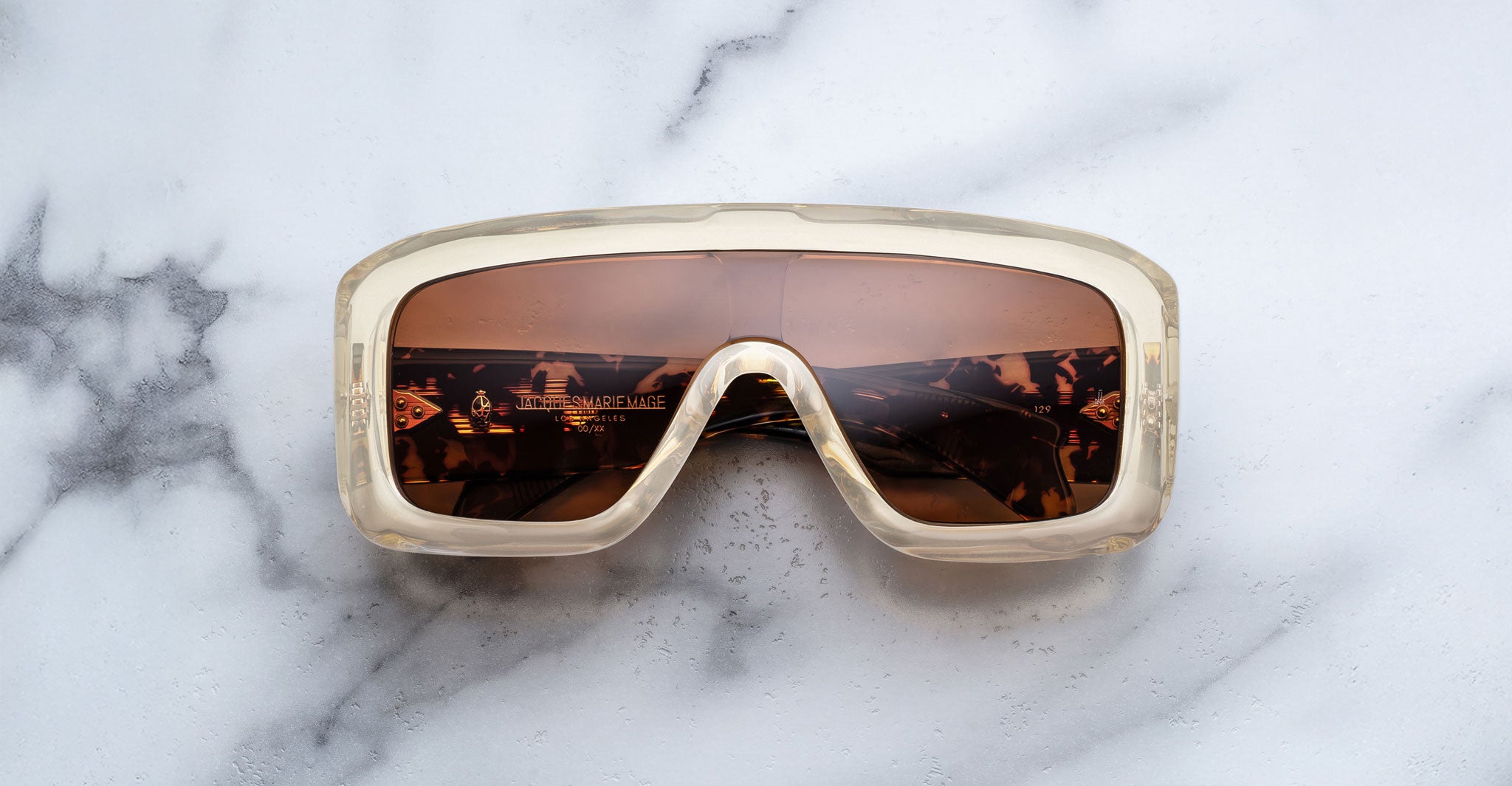 Jacques Marie Mage Pausa sunglasses with beige translucent frames and brown lenses, shown from above.