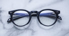 Jacques Marie Mage Percier black eyeglasses with blue arms, top-down view.