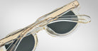 Close-up of Jacques Marie Mage Petrus translucent sunglasses with dark lenses and gold accents, viewed from above on a plain light gray background.
