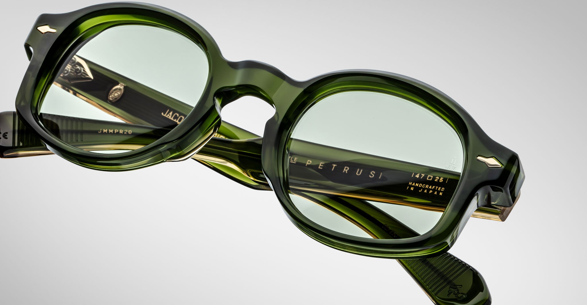 Close-up view of Jacques Marie Mage Petrus green acetate eyeglasses featuring round lenses, thick frames, and visible branding with manufacturing details on the inside of the temple arms.