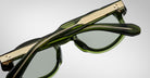 A close-up view of Jacques Marie Mage Petrus sunglasses in green with gold metal temple accents, folded and set against a plain light gray background.