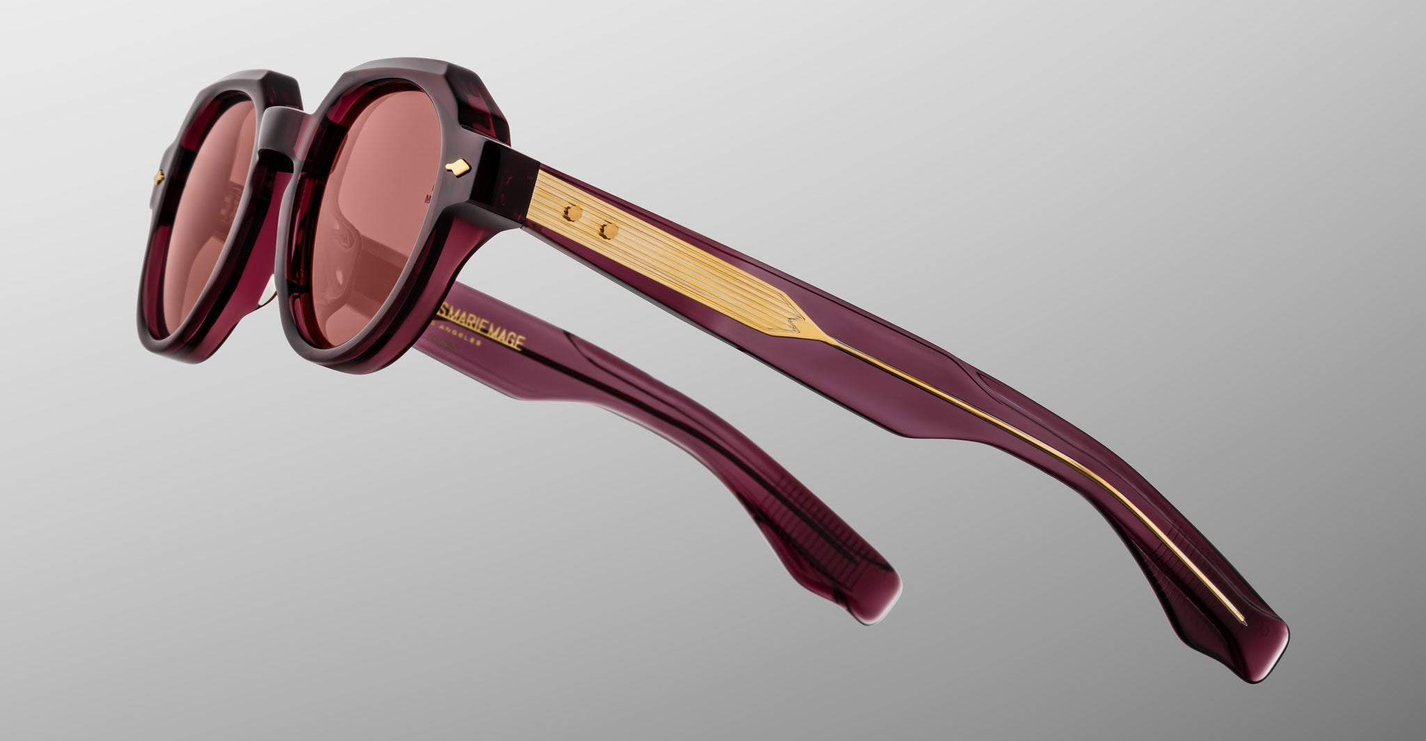 The Jacques Marie Mage Pontian is a pair of maroon geometric sunglasses with gold-accented arms and tinted lenses, displayed against a plain gray background.