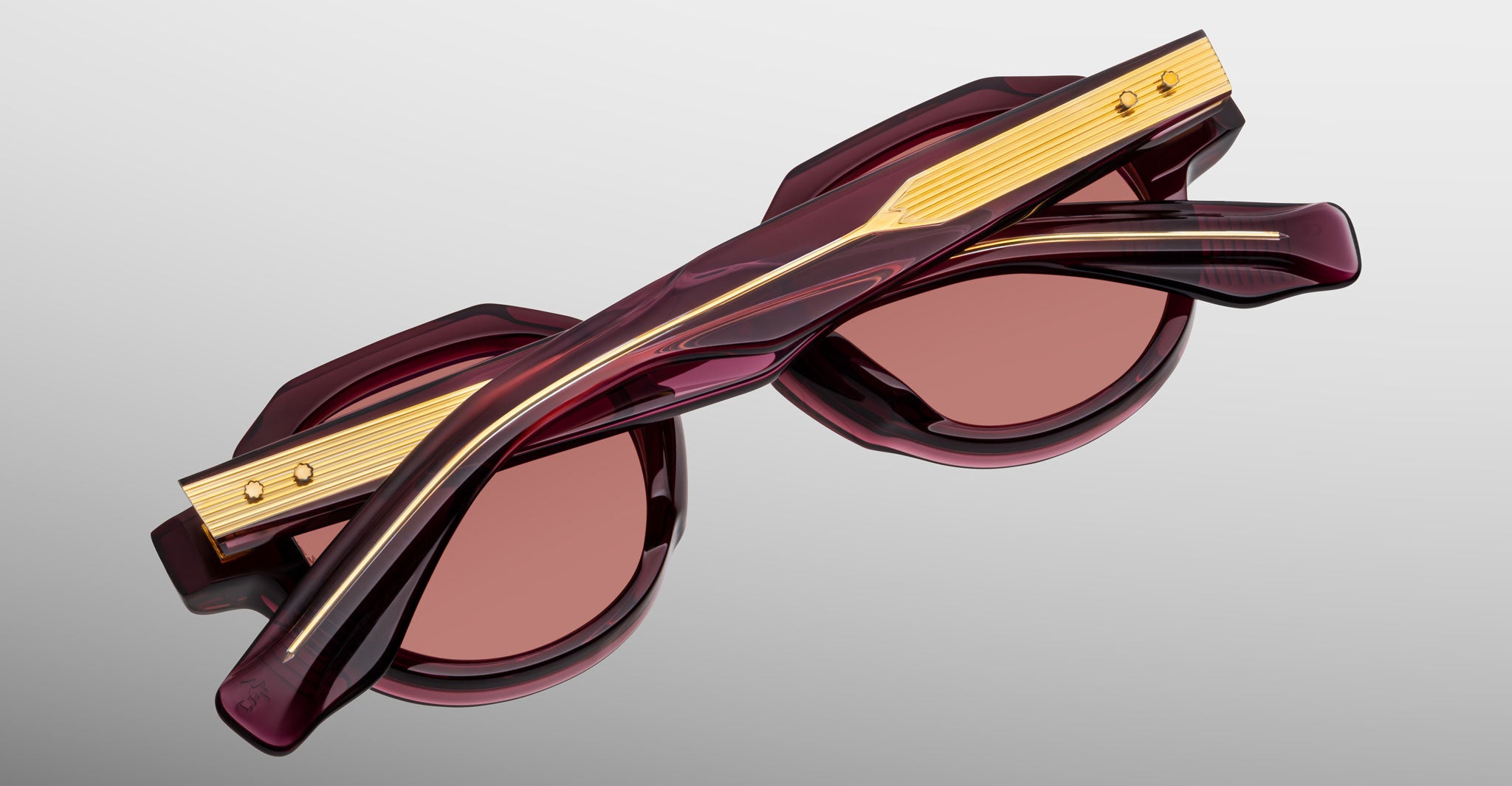 Jacques Marie Mage Pontian sunglasses feature maroon frames, gold temple accents, and brown-tinted lenses, displayed folded from above on a light gray background.
