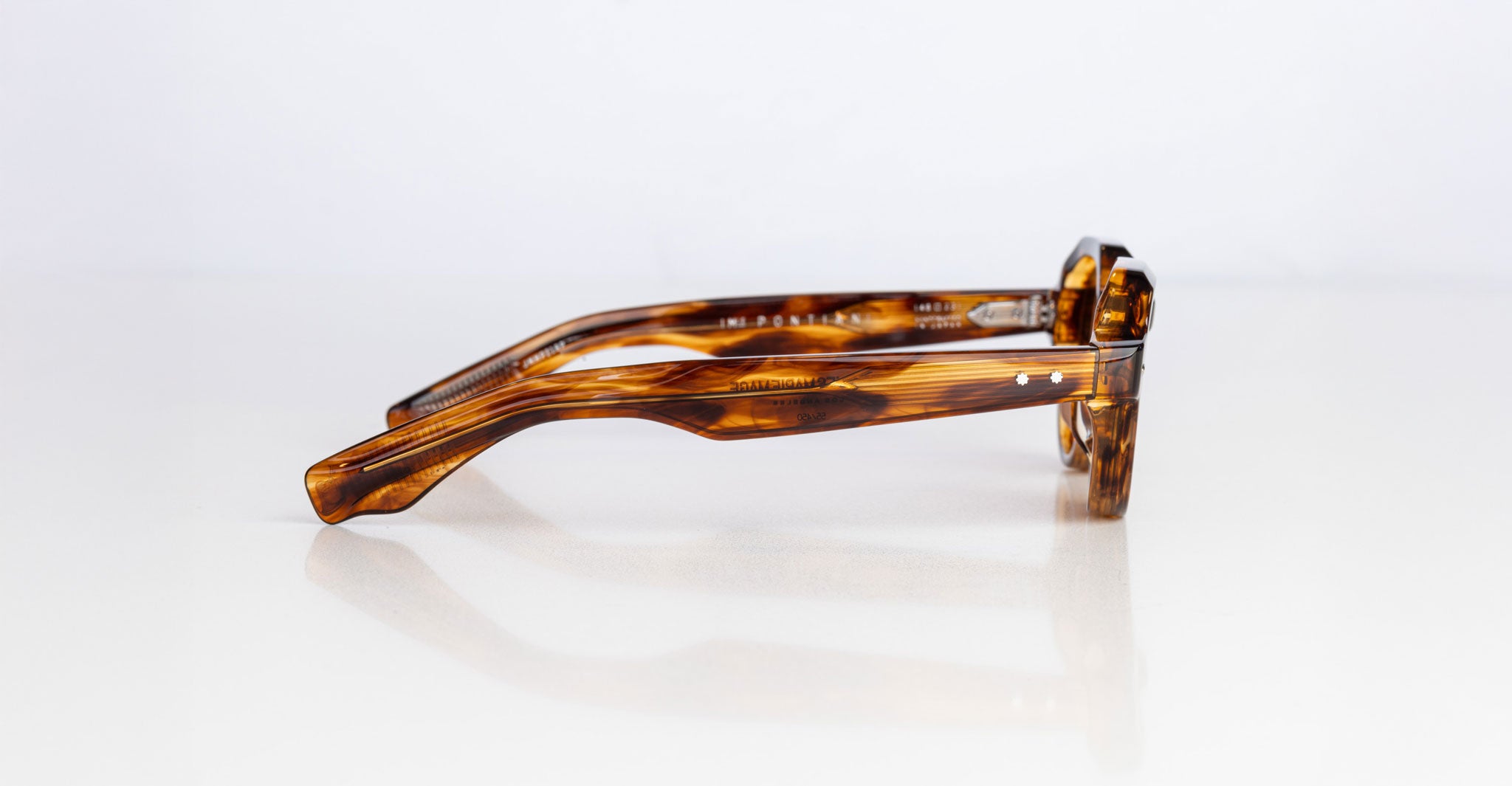 The Jacques Marie Mage Pontian brown tortoiseshell eyeglasses are shown folded on their side on a white surface, with both the arms and frames clearly visible.