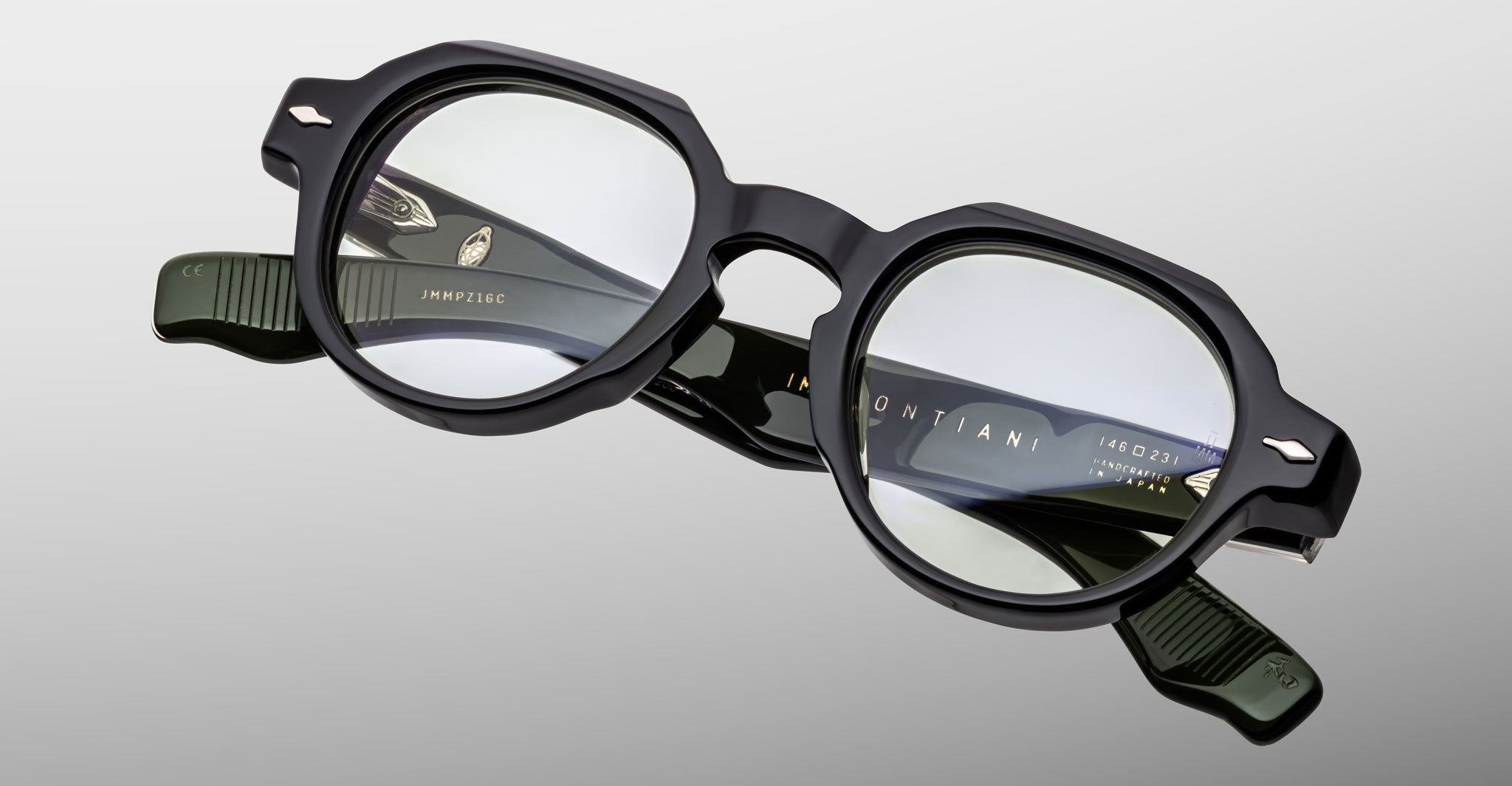 A pair of Jacques Marie Mage Pontian black, thick-rimmed eyeglasses with round lenses and silver hinge accents rests on a light gray background.