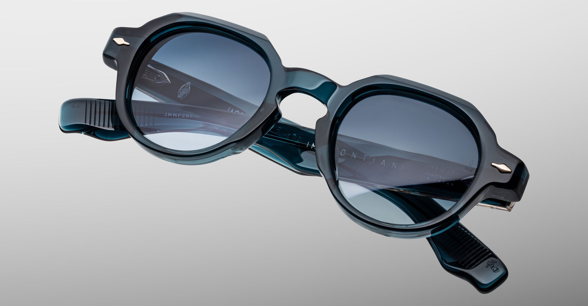 The Jacques Marie Mage Pontian sunglasses, featuring dark round acetate frames and blue-tinted lenses, are shown folded on a light gray surface.