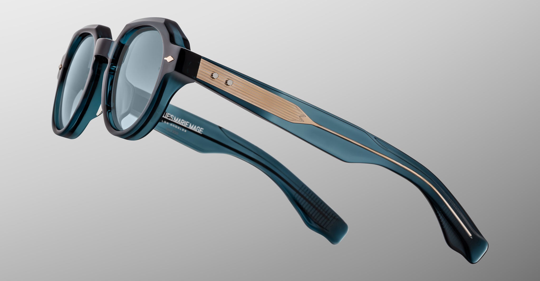 Close-up of Jacques Marie Mage Pontian eyeglasses featuring thick, translucent teal frames, light wood detail on the temples, and clear lenses, displayed against a plain gray background.