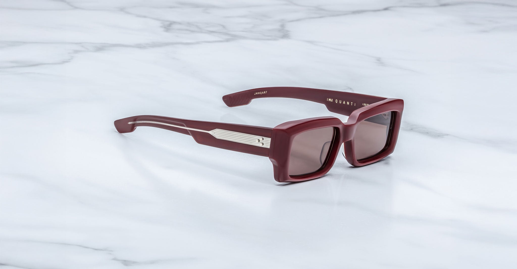 Jacques Marie Mage Quant in Bordeaux Empire, rectangular burgundy acetate sunglasses shown from a side angle, featuring bold sculpted rims, wide temples with signature metal inlay, and softly tinted lenses on a light marble surface.