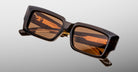 Jacques Marie Mage Quant in London, rectangular translucent brown acetate sunglasses shown from a close angled front view, featuring bold sculpted rims, wide temples, and warm brown tinted lenses.