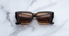 Jacques Marie Mage Quant in London, rectangular translucent brown acetate sunglasses with bold sculpted rims, wide temples, and warm brown tinted lenses, shown front-facing on a light marble surface.