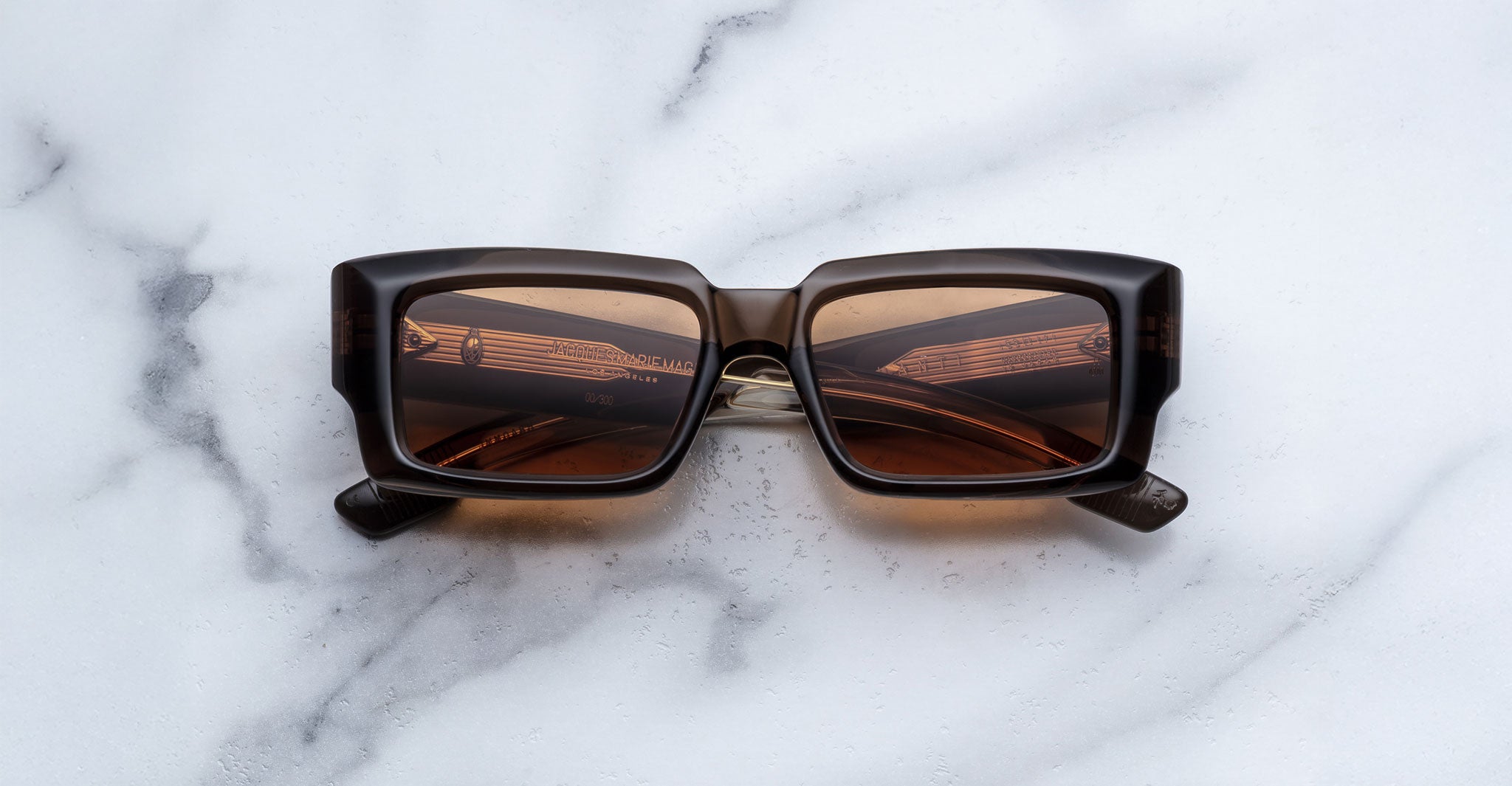 Jacques Marie Mage Quant in London, rectangular translucent brown acetate sunglasses with bold sculpted rims, wide temples, and warm brown tinted lenses, shown front-facing on a light marble surface.